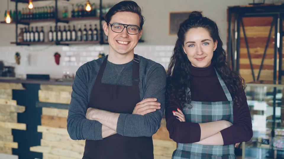 Deux professionnels en tablier, souriants dans leur café